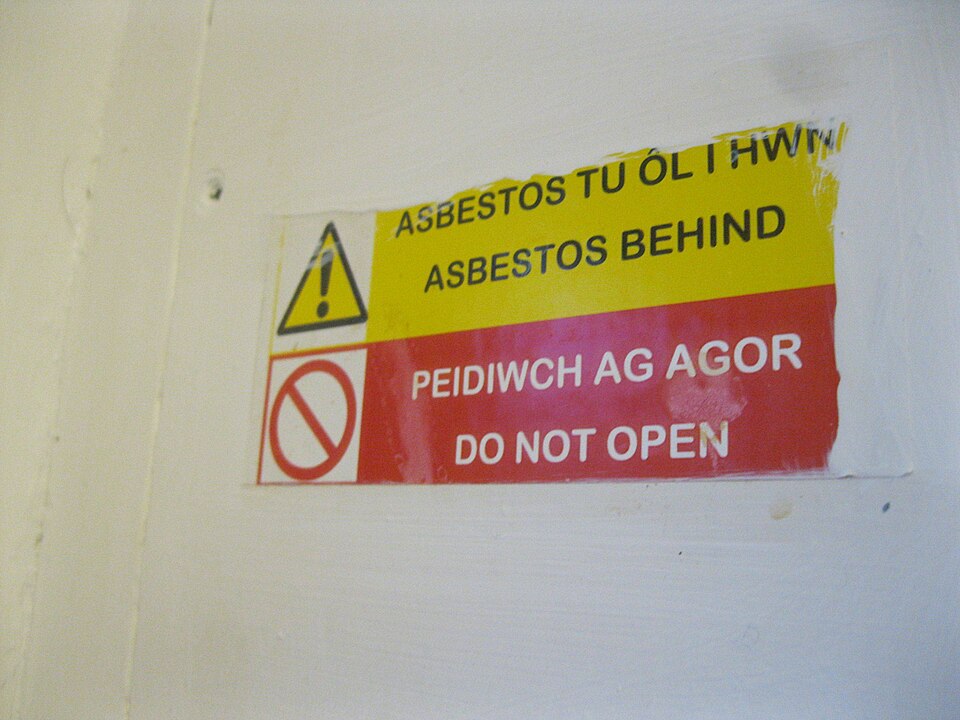 Sign reading 'Asbestos behind, do not open' on a sealed panel