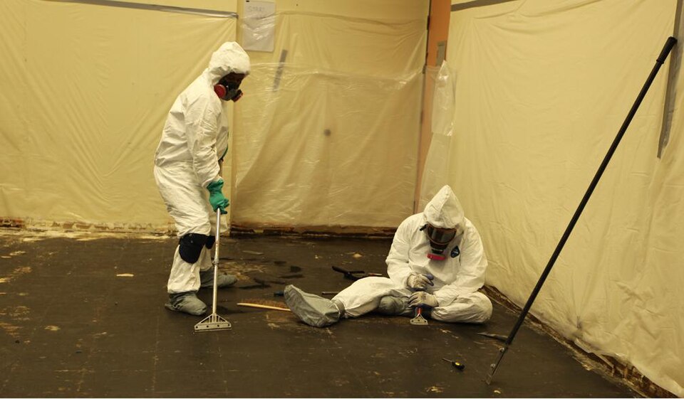 Asbestos removal operatives in protective suits and respirators inside a sealed enclosure